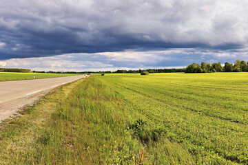 Huge green field next to the road under dramatic clouds