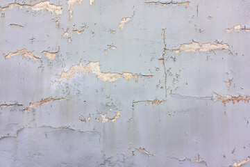 Texture of a cracked and peeling wall showing faded gray paint