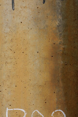 Gradient rust-colored concrete pillar displays signs of wear, with rough finish and small scattered air pocket indentations dotting surface. Partial markings seen at bottom and top of porous cement.