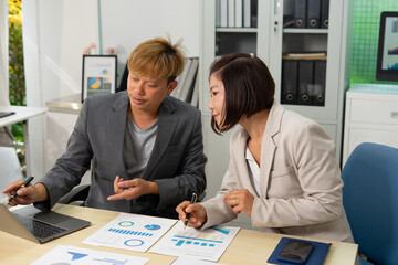 Two business professionals discussing charts in office setting