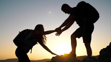 Silhouette of man helping woman conquer mountain at sunset. Representing teamwork, support, worklife balance concepts in business or motivational projects.