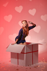 Beautiful girl in a photo studio on a red background in a large white box. Valentine's Day. Photo...