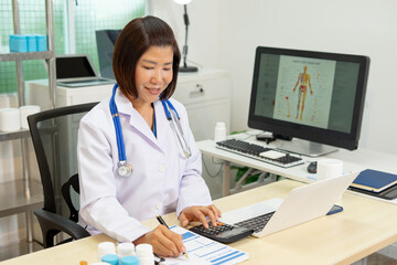 Female doctor working on medical report with calculator and laptop in clinic office