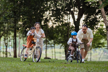 A family of four riding bikes in a park. A man is running to catch up with his children