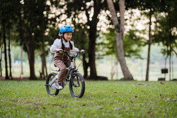 Naklejka premium A young girl is riding a bicycle in a park. She is wearing a helmet and a white shirt