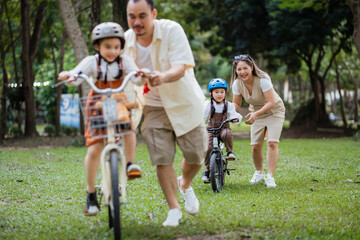 A family of four riding bikes in a park. A man is riding a bike with a child on it