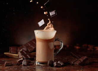 Pieces of bitter chocolate fall in glass mug with cocoa drink.