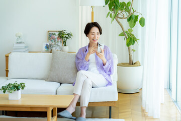 部屋でスマホを操作するミドル女性