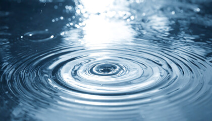 Fresh drop creates concentric ripples in clear blue water surface reflecting light beautifully