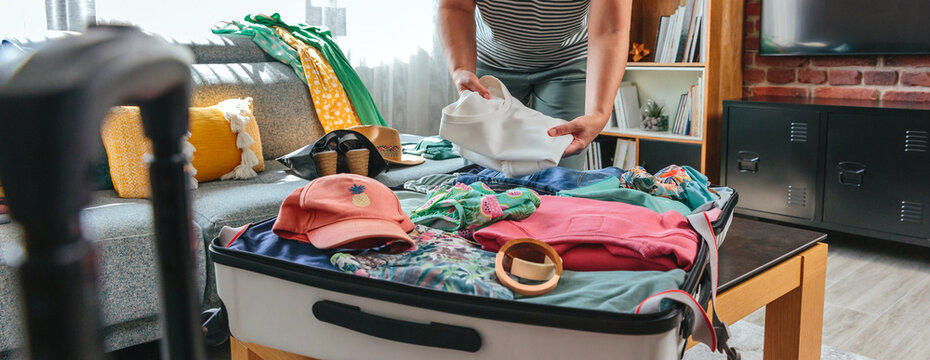 Banner of unrecognizable woman packing clothes into her suitcase with care, preparing for an exciting summer vacation, surrounded by travel accessories and various clothing items, ready for adventure.