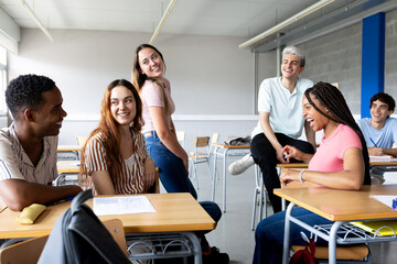 Cheerful high school students chatting and laughing together in classroom