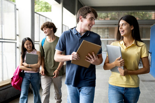Happy college students walking and talking in university hallway