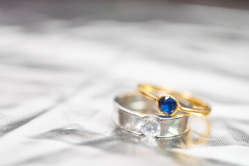 Stacked gold and silver rings set with diamonds and blue sapphires with shiny crumpled metallic...