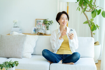部屋でスマホを使うミドル女性