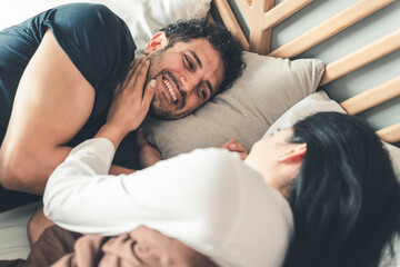 Male and female bonding relationship, Couple lying on bed smiling and holding hands, woman looking...