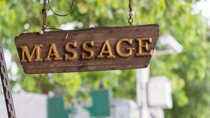 Rustic wooden ‘Massage’ sign hanging outside a leafy Thai street spa
