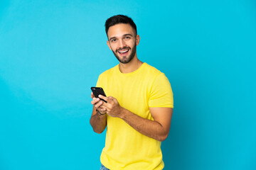 Young caucasian man isolated on blue background sending a message with the mobile