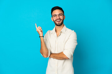 Obraz na płótnie Canvas Young caucasian man isolated on blue background happy and pointing up