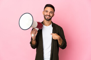 Young caucasian man isolated on pink background holding a megaphone and with surprise facial expression