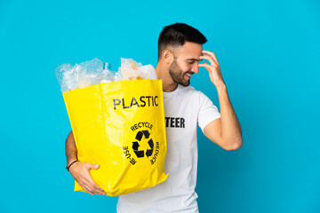 Young caucasian man holding a bag full of plastic bottles to recycle isolated on blue background...