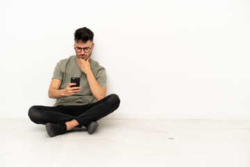 Young caucasian man sitting on the floor isolated on white background thinking and sending a message