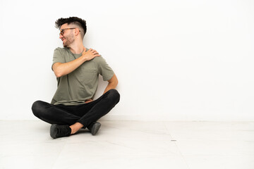 Young caucasian man sitting on the floor isolated on white background suffering from pain in...