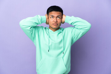 Young Ecuadorian man isolated on purple background frustrated and covering ears