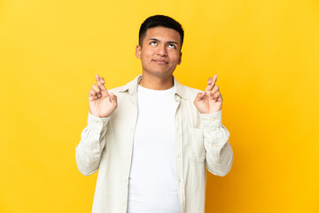 Young Ecuadorian man isolated on yellow background with fingers crossing and wishing the best