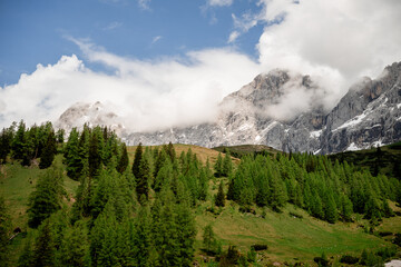 Dramatic Dachstein mountain peaks with lush green valley and clouds in Austria