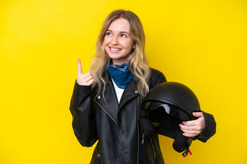 Blonde English young girl with a motorcycle helmet isolated on yellow background pointing up a...