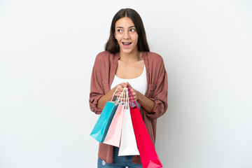 Young French girl isolated on white background holding shopping bags and surprised