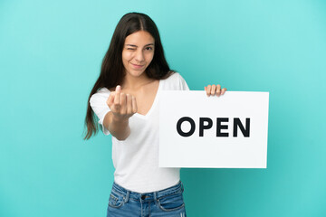 Young French woman isolated on blue background holding a placard with text OPEN and doing coming...