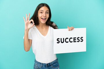 Young French woman isolated on blue background holding a placard with text SUCCESS and celebrating...
