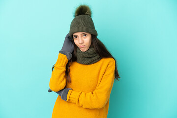 Young French girl isolated on blue background with winter hat having doubts