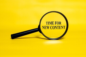 TIME FOR NEW CONTENT concept zoomed through a magnifying glass isolated on a yellow background. 