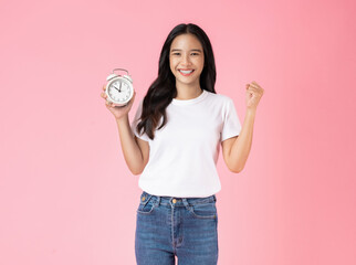 Young asian woman holding alarm clock and smiling isolated on pink background studio.