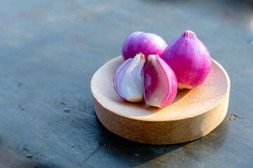 Fresh red shallots on a wooden plate, with some halved to reveal vibrant layers, placed on a rustic textured surface