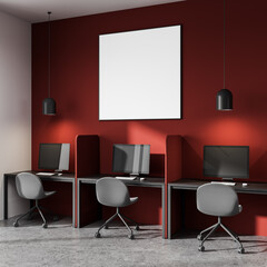 Blank poster mockup on red wall above modern computer workstations in minimal office interior with...