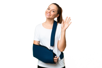 Young blonde woman with broken arm and wearing a sling over isolated chroma key background saluting with hand with happy expression
