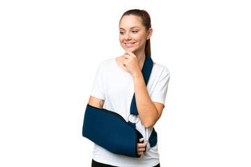 Young blonde woman with broken arm and wearing a sling over isolated chroma key background looking...