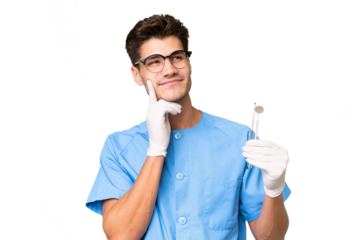 Young dentist man holding tools over isolated background thinking an idea while looking up