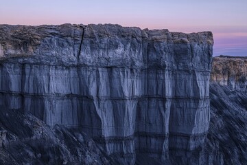 A towering cliff face, layered with sedimentary rock, shows the passage of time and geological...