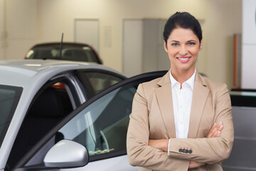 Female professional in blazer standing beside silver sedan with open door in showroom, copy space