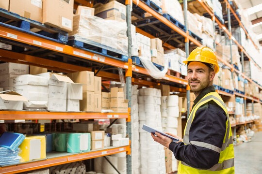 Male worker wearing hard hat and hi-vis vest inspecting stock with tablet in warehouse, copy space - Powered by Adobe