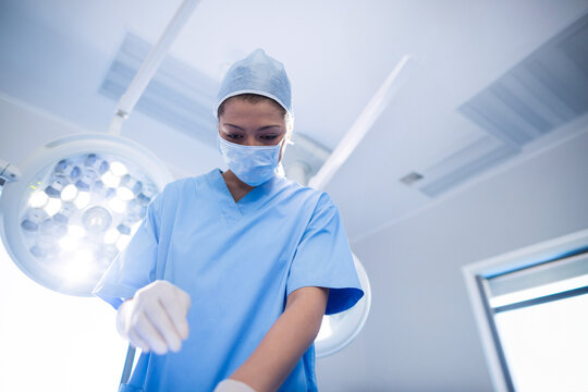 Female surgeon in blue scrubs leaning under surgical lights in operating room preparing instruments