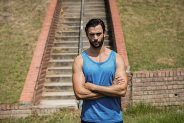 Male athlete standing before concrete staircase flanked by brick walls on grass slope in sunlight
