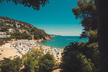 Blanes, Spain - 06.2025 - Panoramic view of Cala Bona beach with sunbathers relaxing under sun umbrellas over the Mediterranean Sea.
