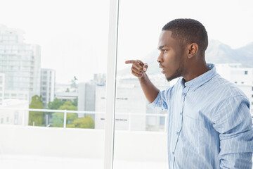 African American man in blue shirt standing by glass window pointing at urban buildings, copy space