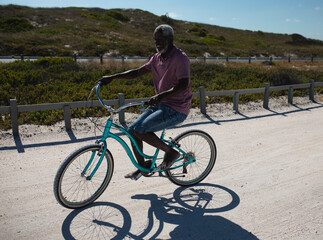Mature African American man riding turquoise cruiser bicycle along coastal trail beside rail fence