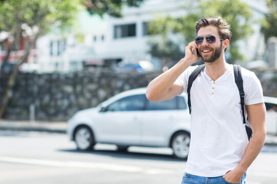 Man in his twenties calling on smartphone on sidewalk by stone wall wearing sunglasses, copy space